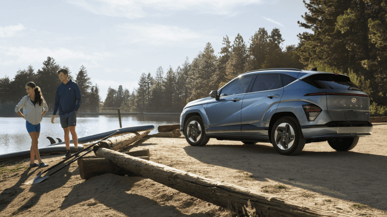 2025 EV Kona parked in nature near lake with couple walking away from car down beach